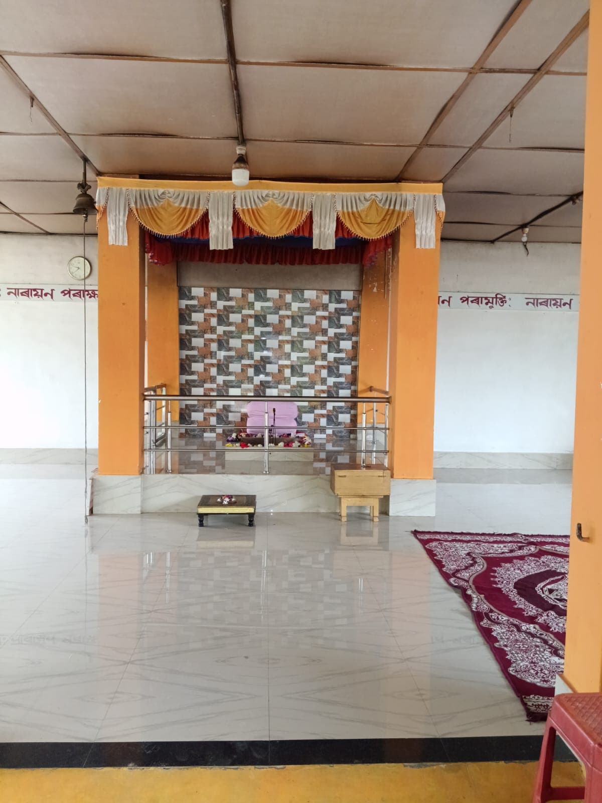 A wide tiled hall with an altar framed in orange pillars at the far end and a patterned rug on the floor