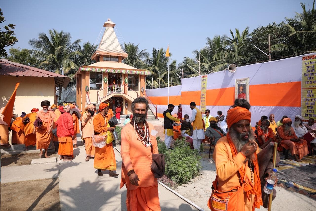 People in saffron robes and turbans gathered on a paved courtyard in front of the tiered temple and orange-and-white tents