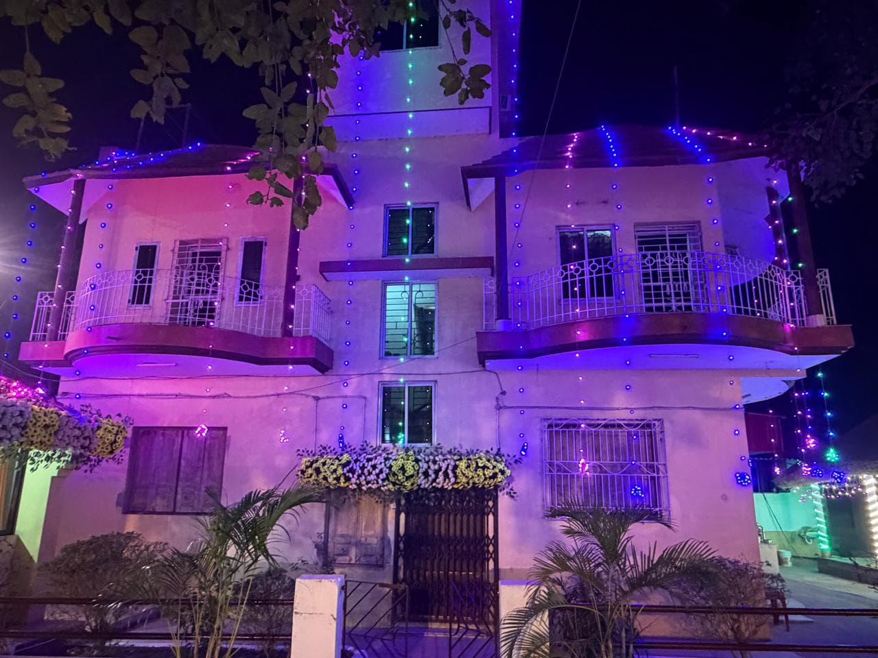 A two-storey building lit in purple and pink with strings of coloured lights at night