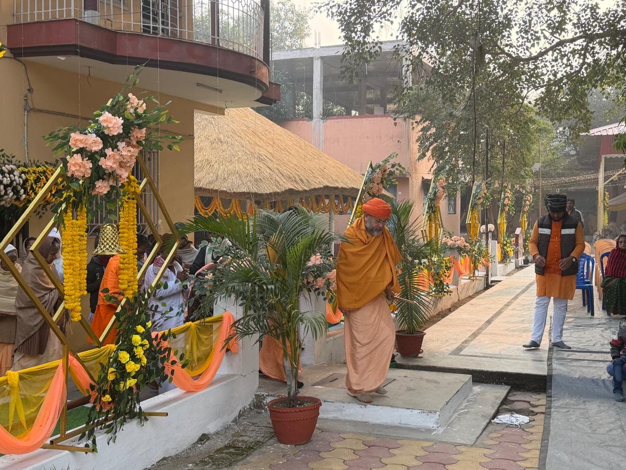 A walkway decorated with flower arrangements and saffron drapery, with people in saffron robes walking along it