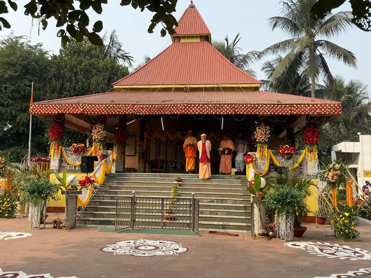 A temple pavilion with a tiered red roof and a broad flight of steps, decorated with garlands