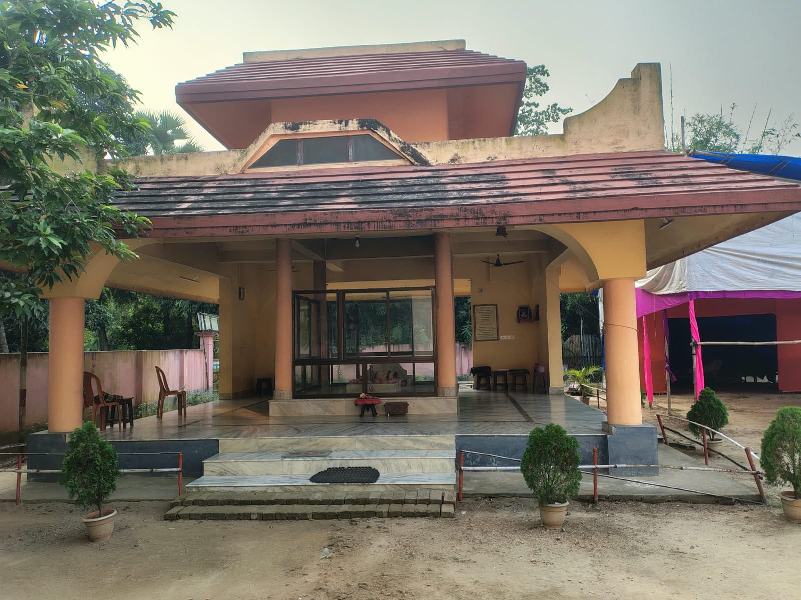 A pavilion with a tiled roof and pillared veranda, with potted shrubs at the foot of its steps