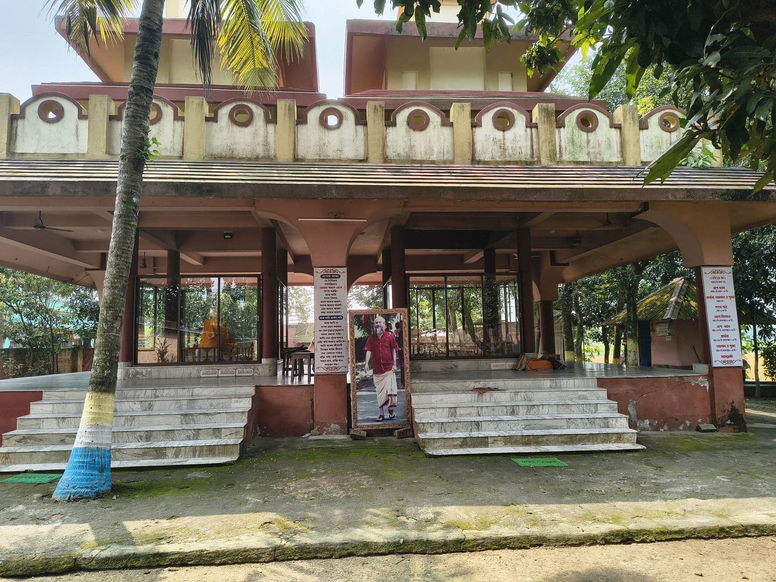 The front of a temple with an open pillared hall and twin flights of steps, framed by palm trunks