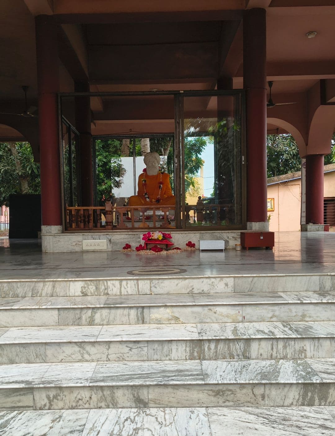 Marble steps rising to a glass-walled shrine with a seated saffron statue inside an open hall
