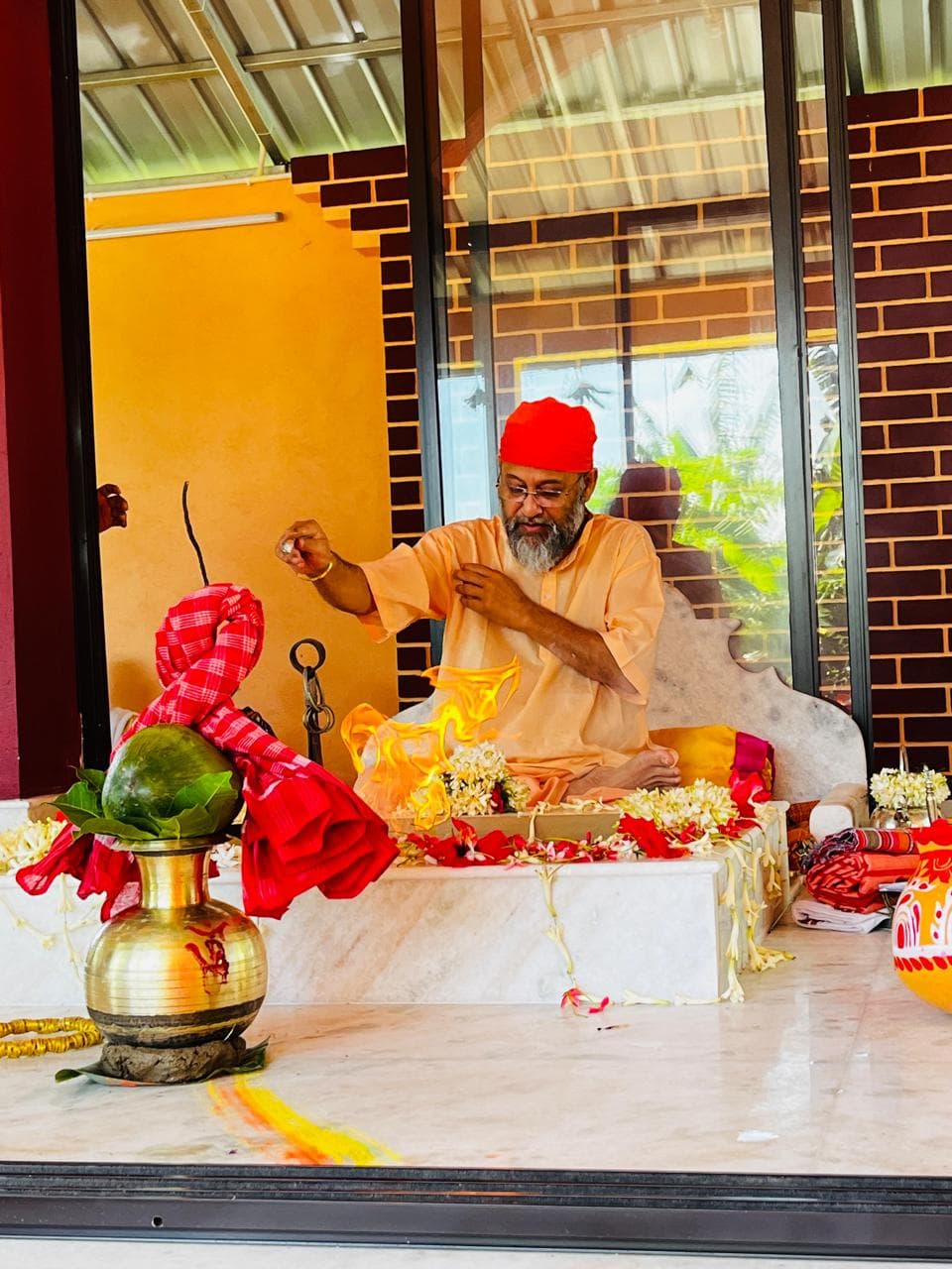 A man in a red turban and saffron clothing performing a ritual at a marble altar with a brass pot