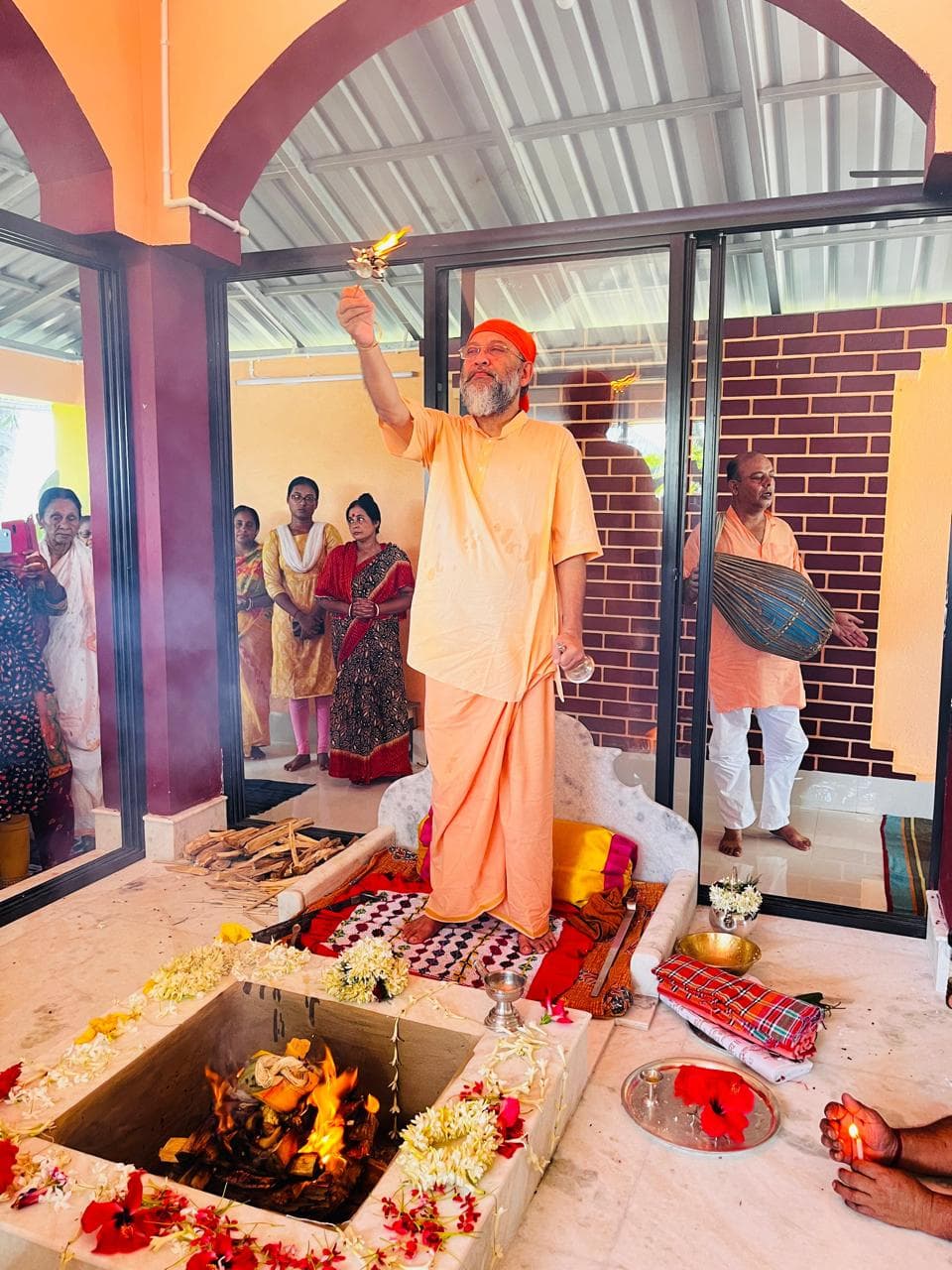 A man in saffron raising a flame in a ritual beside a sacred fire, with others watching