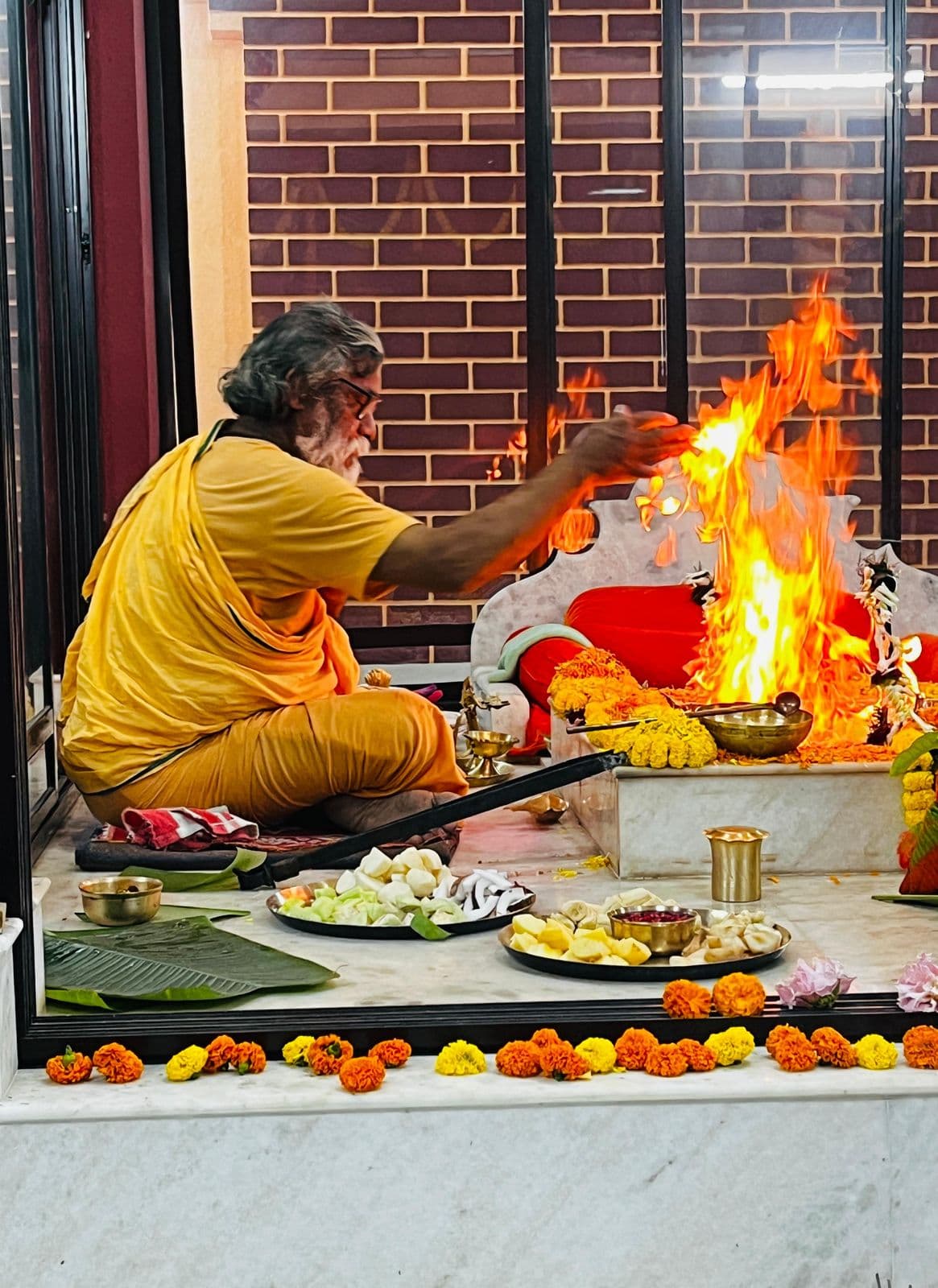 A man in saffron making offerings into a blazing sacred fire on a marble altar laid with flowers