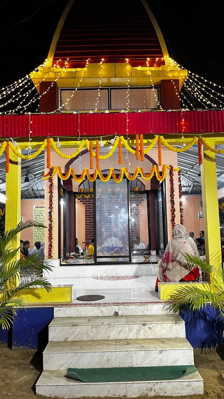 A temple outlined in strings of lights at night, hung with marigold garlands above its steps