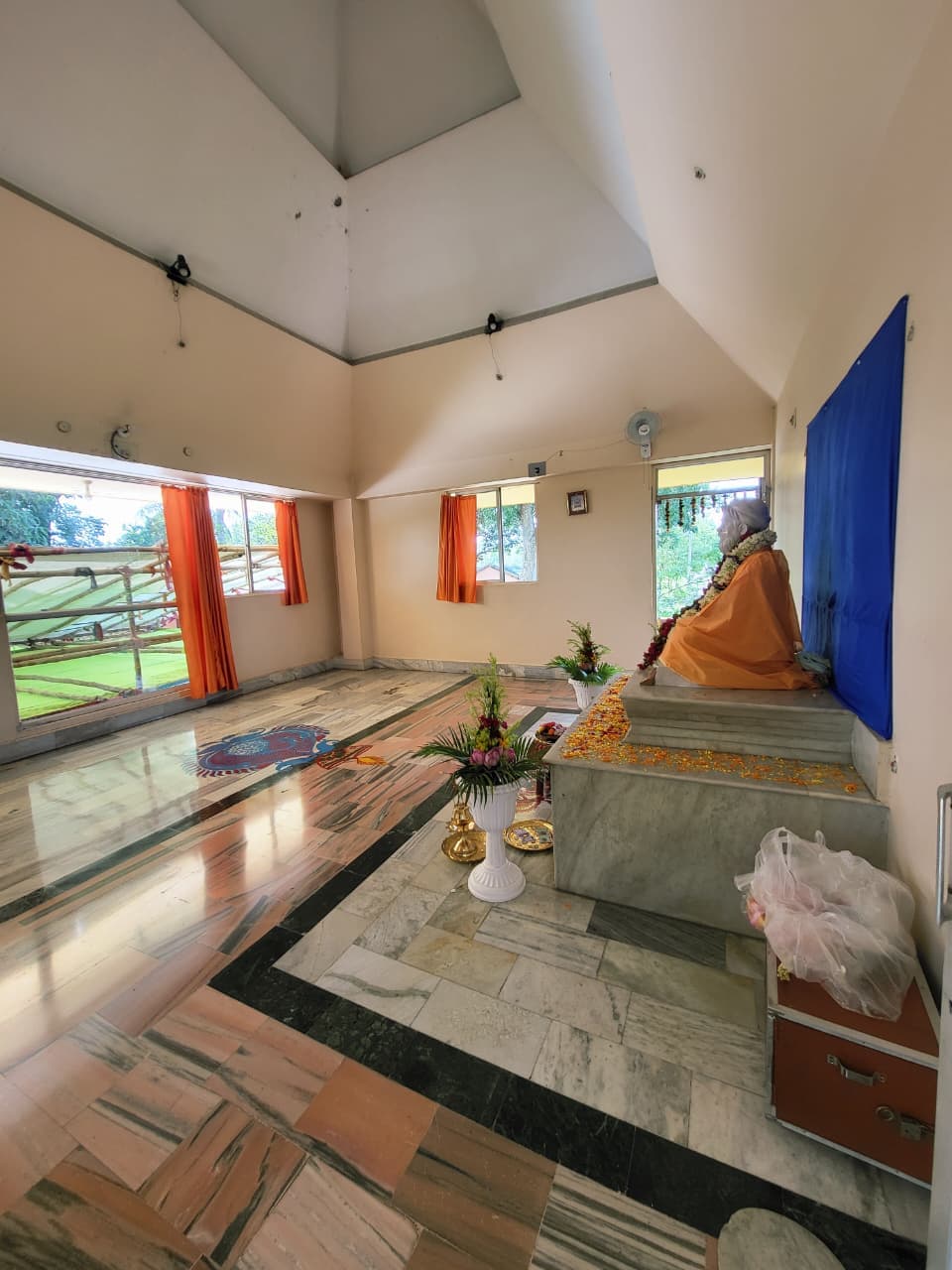 A wide view of a bright hall with marble floors and a garlanded seated statue against a blue backdrop