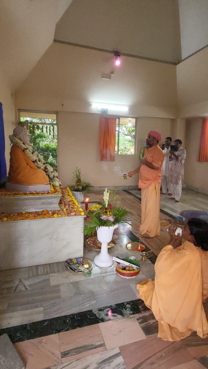 A hall with a seated statue on a marble platform, with people in saffron moving about in front of it