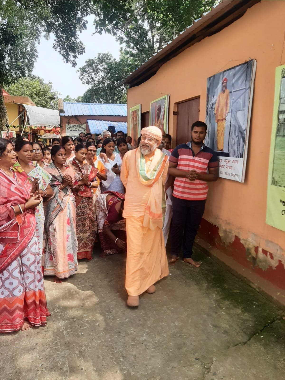 A man in saffron robes walking beside a line of women holding lamps outside a building hung with portraits