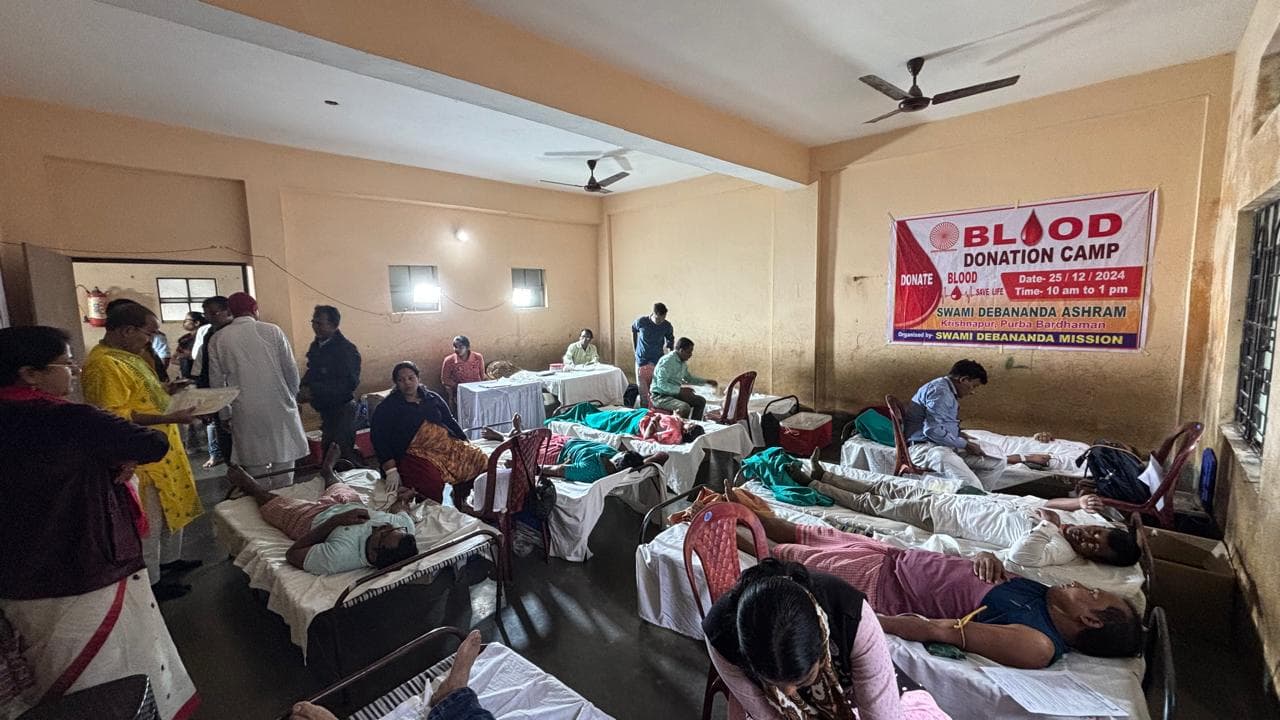 A blood donation camp: donors resting on beds in a hall, with a banner on the wall