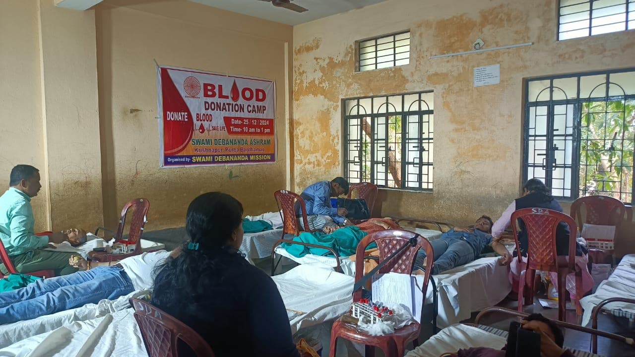 A blood donation camp: donors resting on beds in a hall, with a banner on the wall