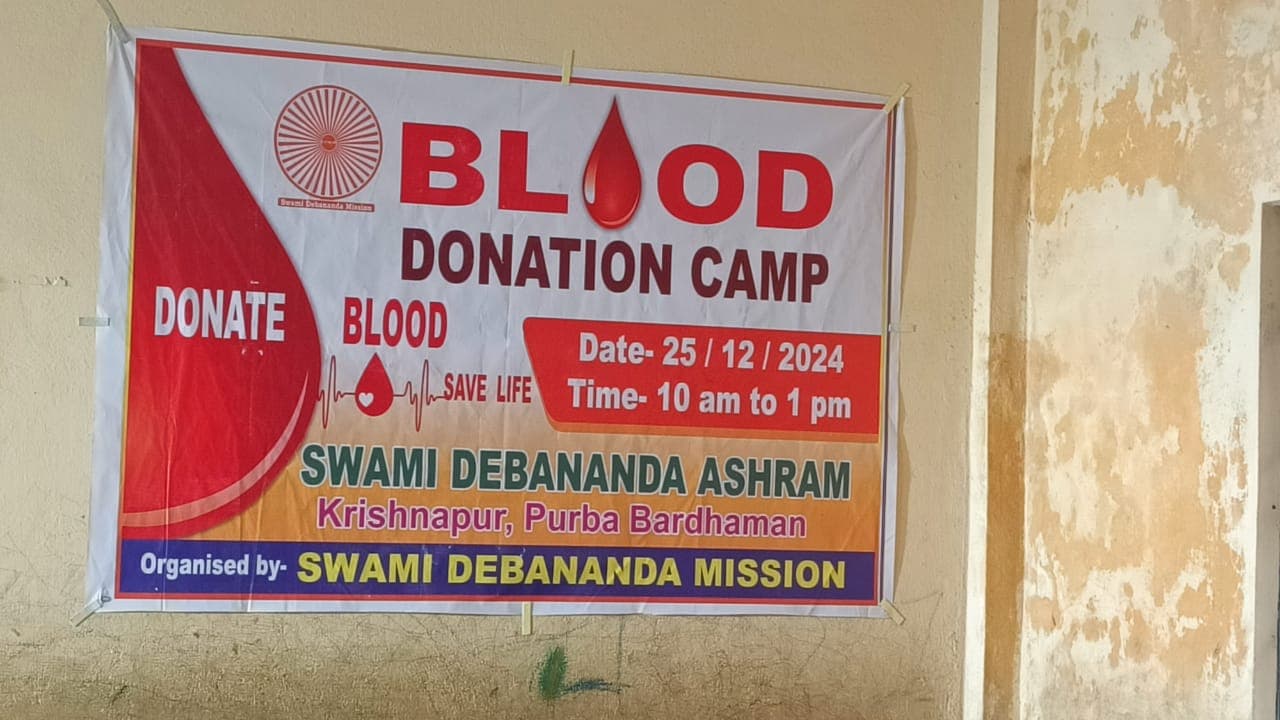 A blood donation camp: donors resting on beds in a hall, with a banner on the wall