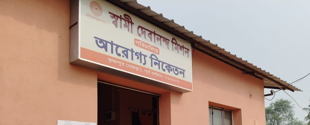 A dispensary building with a tin-roofed porch and a signboard lettered in Bengali above the door