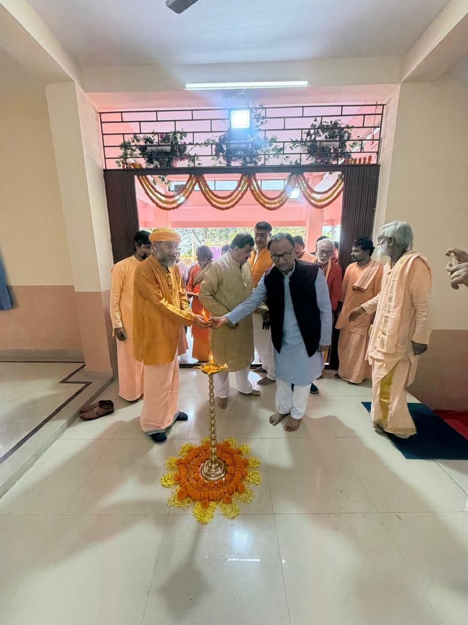 Monks and guests standing round a lamp and a ring of marigolds in a corridor