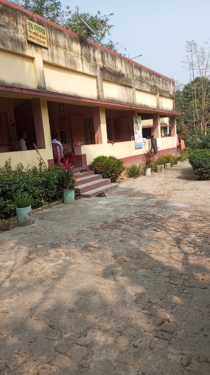 A paved path running along a two-storey building with a covered veranda and flowering shrubs