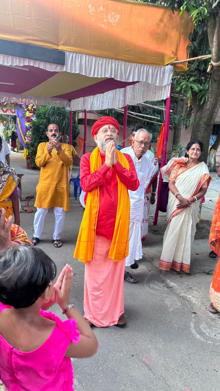 Swami Debananda Maharaj standing with palms joined in greeting beneath a decorated canopy