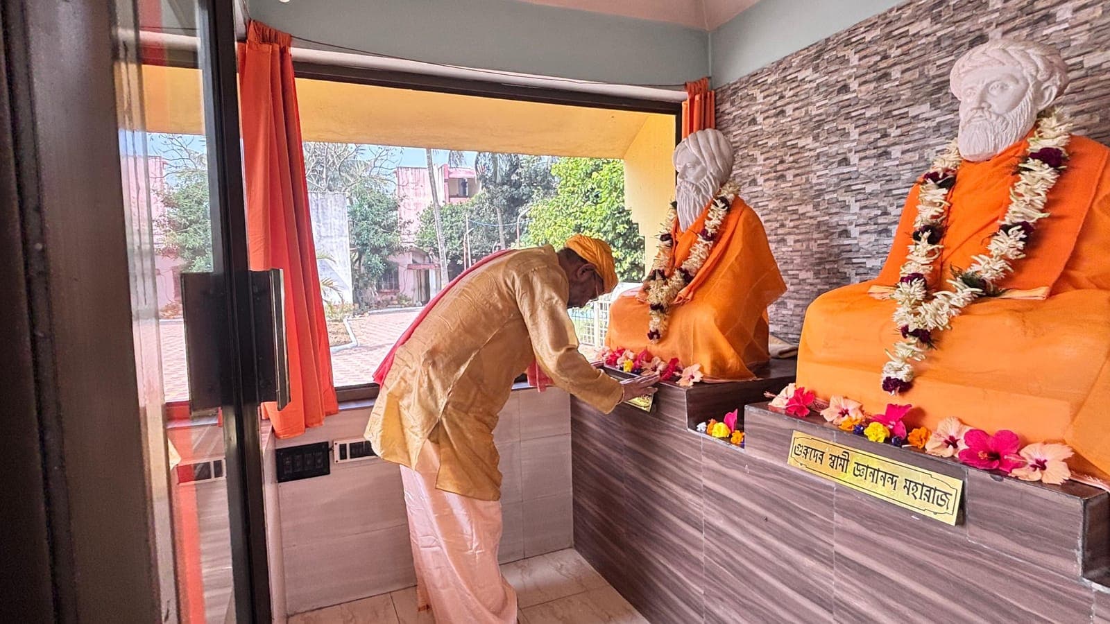 Swami Debananda Maharaj offering flowers before two garlanded statues of saints