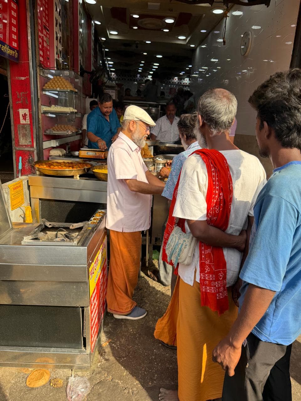 A man in a cap standing at a food stall, with people waiting in front of the counter