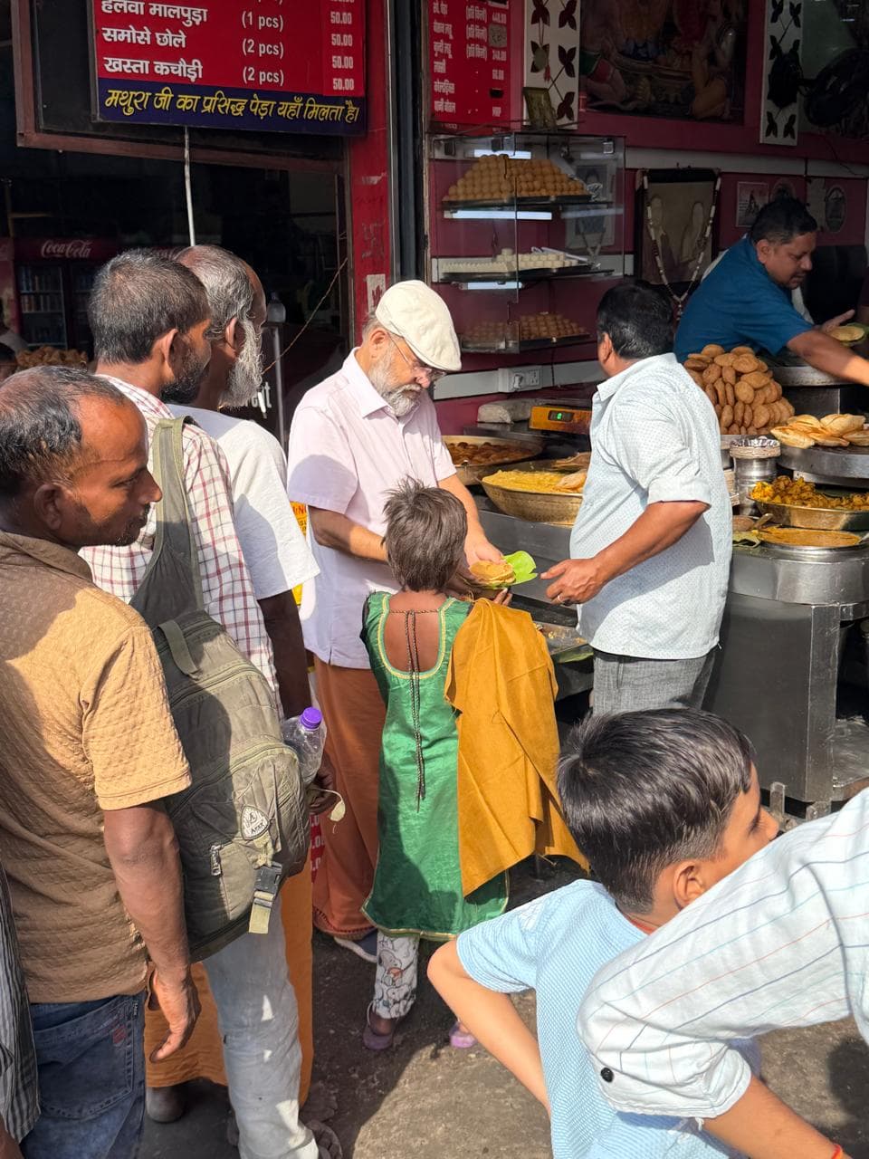 A man in a cap at a crowded food stall, with people gathered at the counter