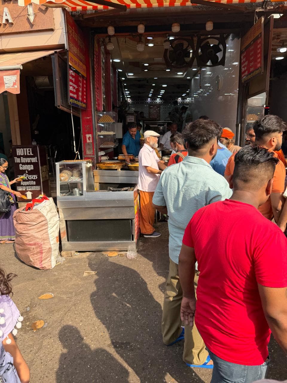 A busy street-side food stall with people queueing at its counter
