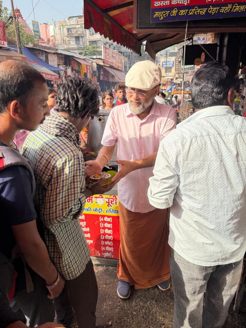 A man in a cap and pink shirt handing out food among a crowd at a street stall