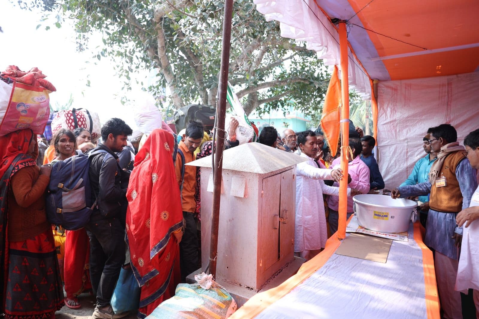 People queueing beneath an orange-and-white canopy where food is being served from large pots