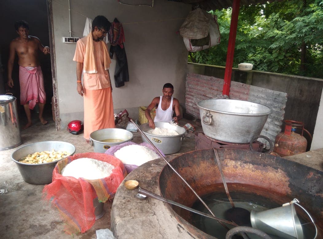 An outdoor kitchen with a large cooking pot, bowls of rice and two cooks at work