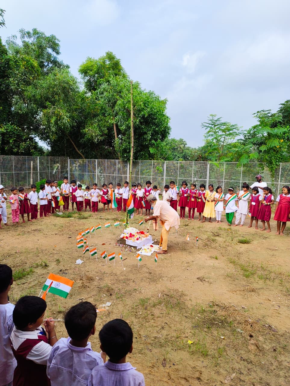 Students in uniform standing in a wide circle around a flag-decorated design on the ground