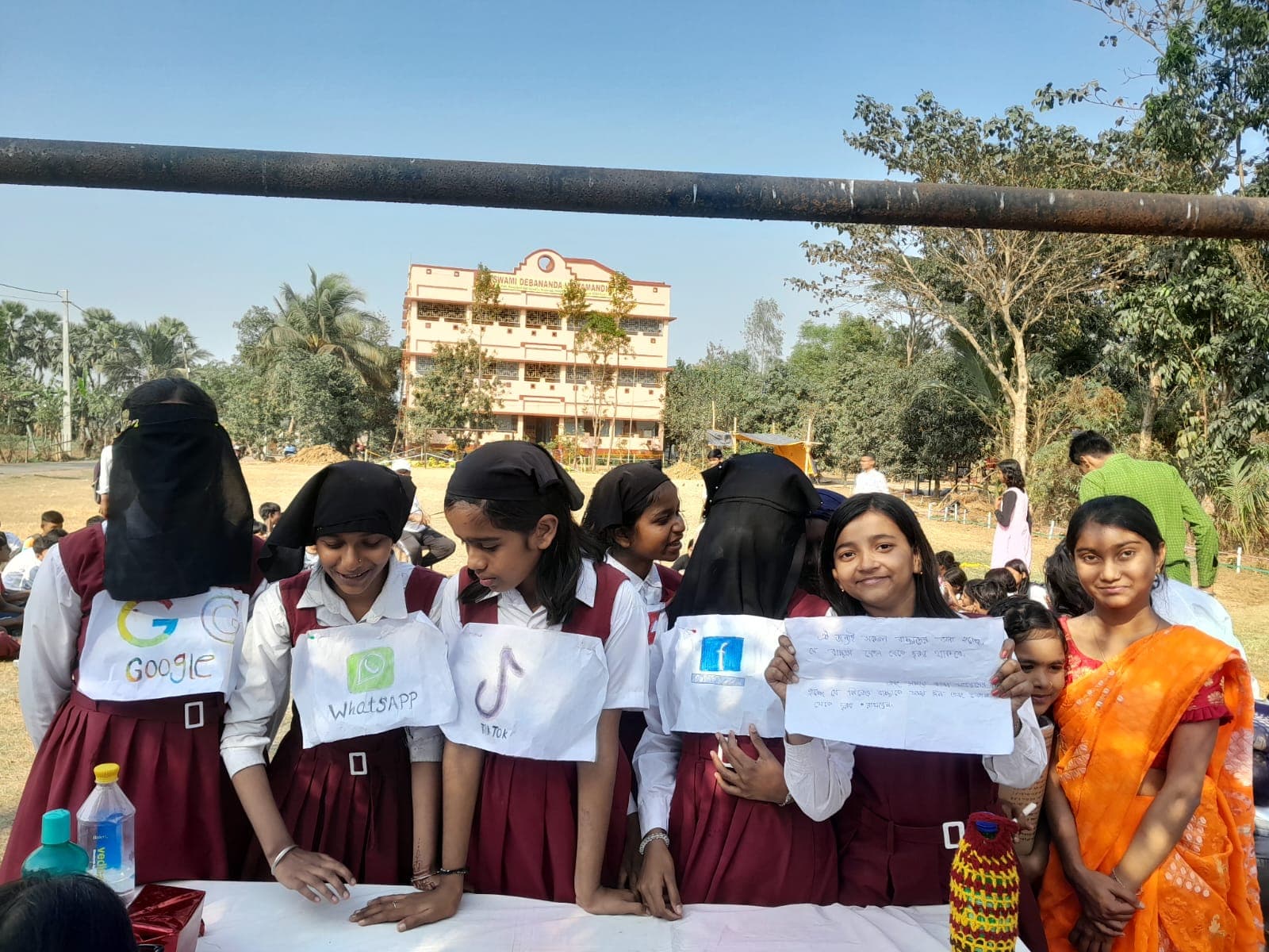 Schoolgirls in uniform at a table holding up handmade signs, with the school building in the distance
