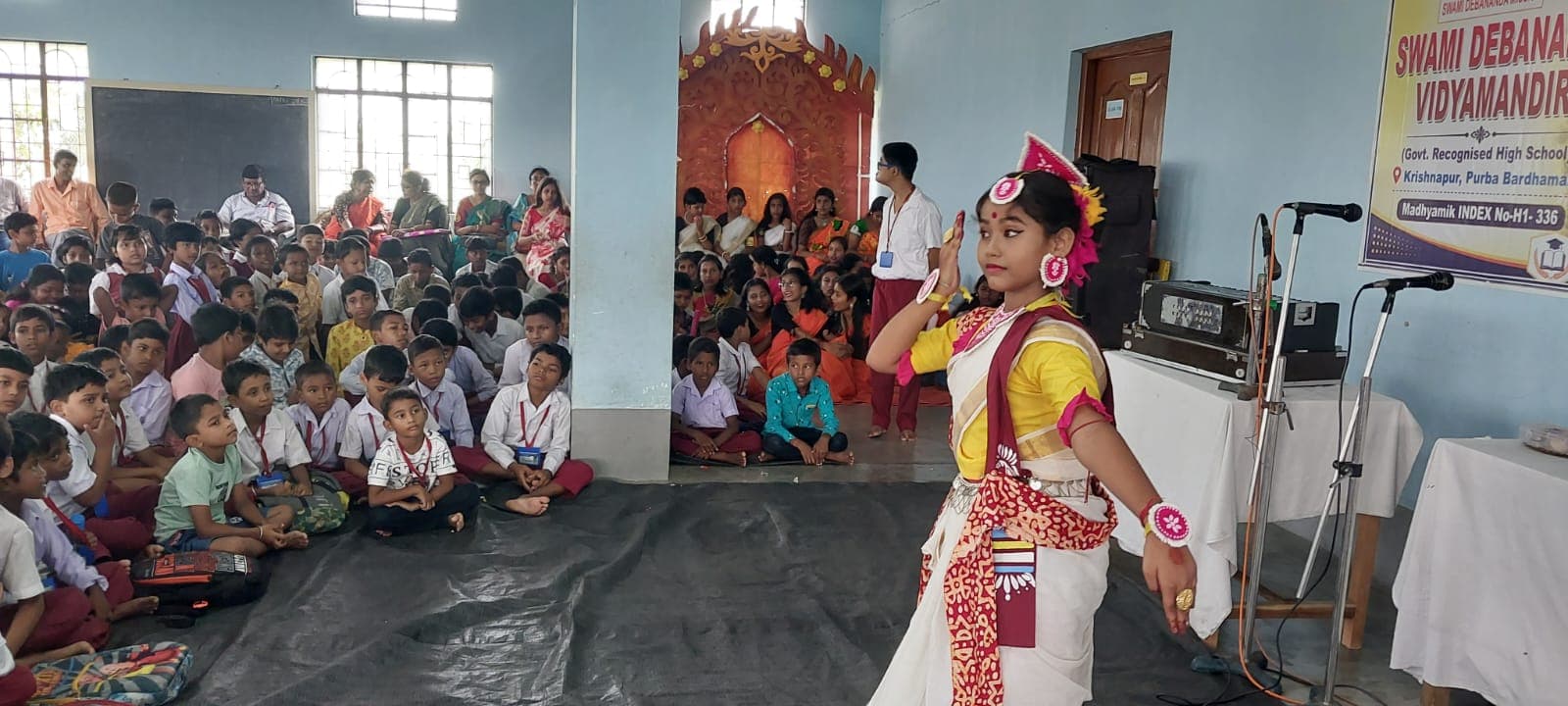 A dancer in costume performing before students seated on the floor of a hall