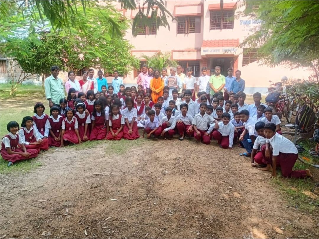 A large group of students and teachers gathered on a lawn in front of a pink school building