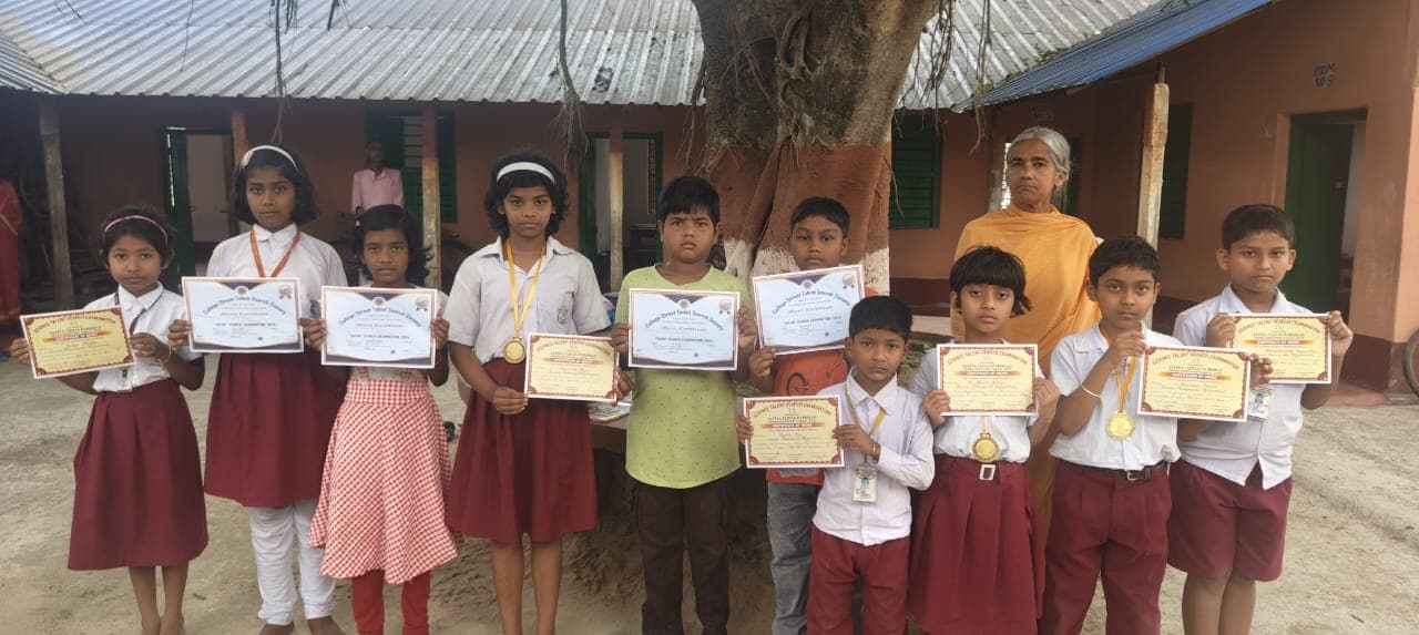 A row of students in uniform holding up certificates in front of a tin-roofed building